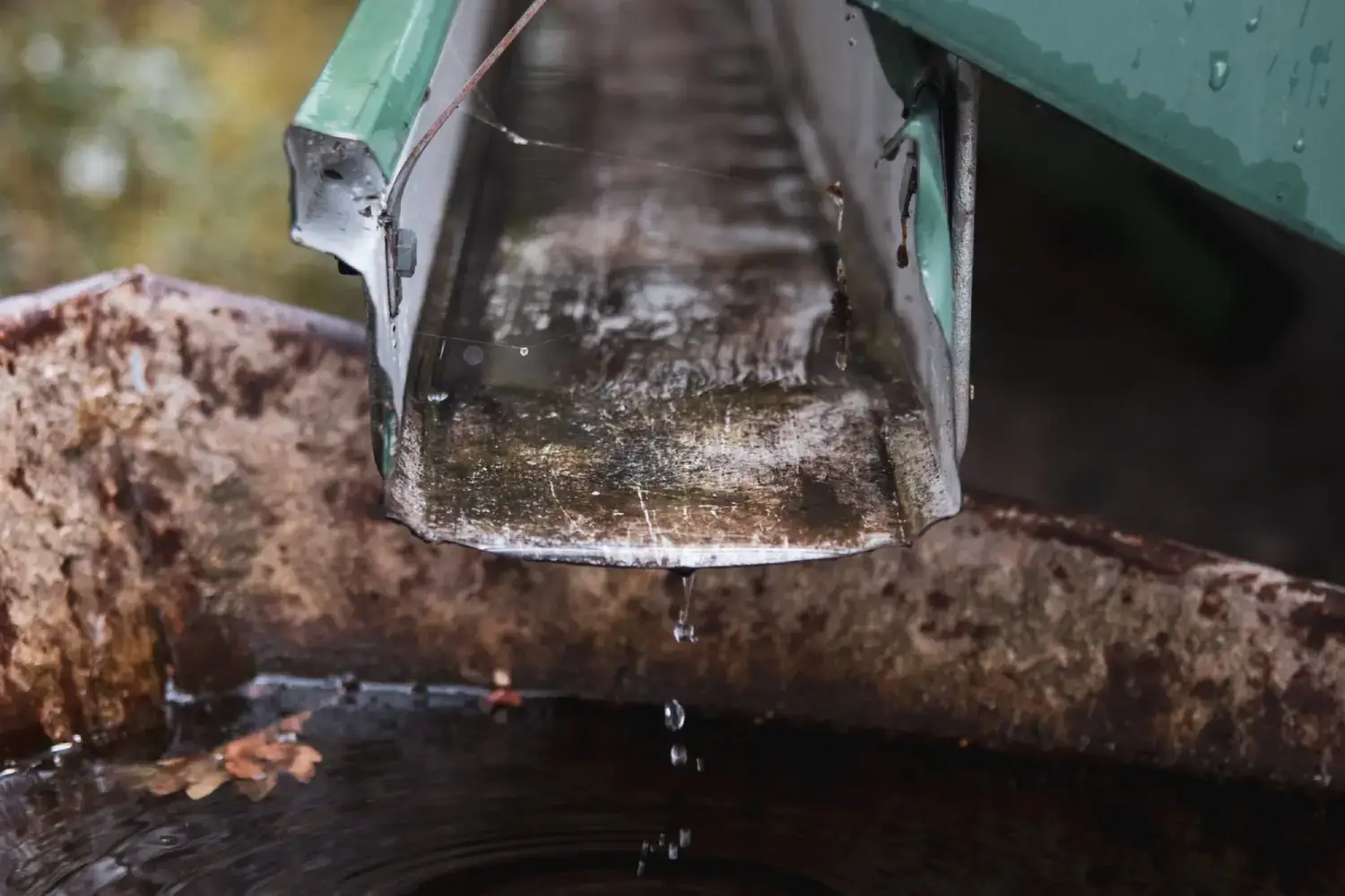 Water pipe runs down a metal gutter, showing early signs of gutter damage.